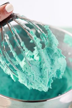 a whisk being used to mix blue and green icing in a bowl