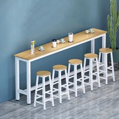 four stools and a long table with cups on it in front of a blue wall