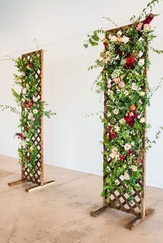 three wooden poles with flowers and greenery on them in the middle of a room