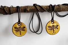 three gold dragonfly pendants hanging from a tree branch with leather cord attached to them