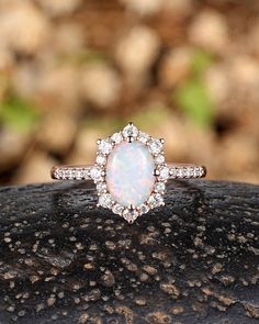 a white opal and diamond ring sitting on top of a rock