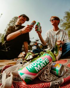 two men sitting next to each other with cans of soda and noodles in front of them