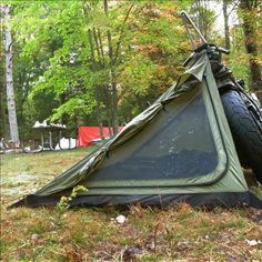 a tent with a motorcycle tire attached to it sitting in the grass next to some trees