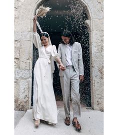 a newly married couple walking out of an open doorway with their hands in the air