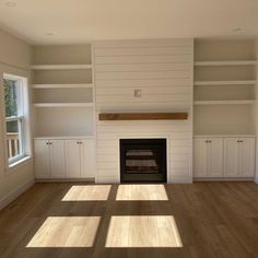 an empty living room with white bookcases and a fireplace in the center,