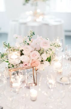 the centerpieces on this table are filled with white and pink flowers, candles, and greenery