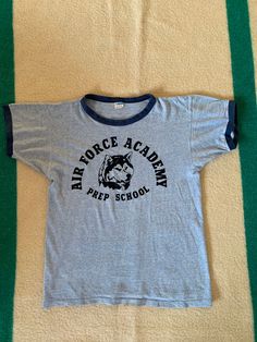 A Vintage Champion Blue Bar Ringer t shirt. US Air Force Prep School graphic with Husky mascot. Made in USA, cotton blend. A few holes, shown in photos. Previous owners name written on the inside of the hem. Collar is a little loose. Size marked large but please refer to the actual measurements: 19 inches from pit to pit measured lying flat, 19 inches across the shoulders and the overall length is 25 inches. Cotton T-shirt With Letter Print For Fan Conventions, Retro Crew Neck T-shirt For School, School Crew Neck T-shirt With Logo Print, Band Merch Cotton Tops For School, Cotton Band Merch Tops For School, School Cotton Tops With Band Merch Style, School Tops In Cotton With Band Merch Style, Cotton T-shirt With Text Print For Fan Conventions, Retro Cotton T-shirt For Fan Gear