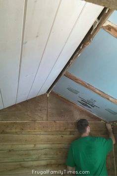 a man in green shirt working on an unfinished ceiling with wood paneling and insulation