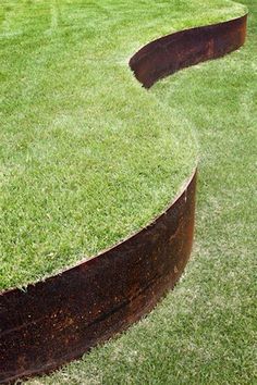 a large metal sculpture on top of green grass in the shape of an arrow with two long curved sections