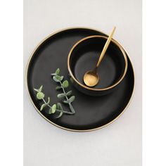 a black and gold plate with a spoon on it, sitting next to a small plant