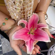 a woman is holding a pink flower in her hand and bracelets on her wrist