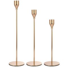 three gold candlesticks on white bases with one candle in the middle and one standing upright