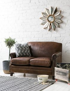 a brown leather couch sitting next to a white brick wall with a clock above it