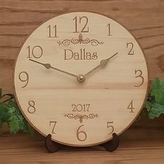 a wooden clock sitting on top of a table next to green leaves and ivys