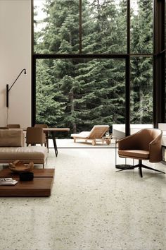 a living room filled with furniture next to large windows covered in lots of forest trees