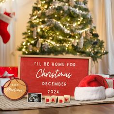 a christmas sign sitting on top of a wooden table next to a christmas tree and presents