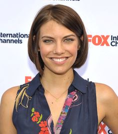 a woman with short brown hair wearing a blue shirt and smiling at the camera while standing in front of an international channel logo