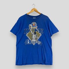 a blue t - shirt hanging on a wooden hanger with the words duke in it