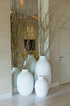 three white vases are sitting on the floor in front of a mirror with bare branches