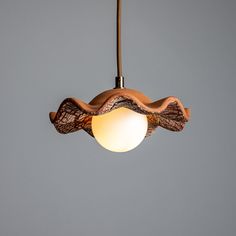 a wooden light hanging from a ceiling with a white ball in the foreground and a gray wall behind it