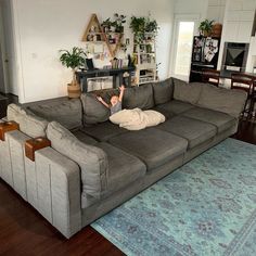 a man laying on top of a gray couch in a living room next to a blue rug