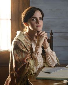 a woman sitting at a table with a book and pen in front of her face