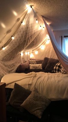 a bed with some lights hanging from it's ceiling and pillows on the floor