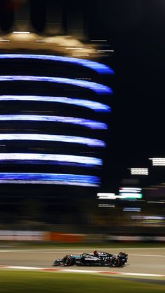 a racing car driving down the track in front of a large building with blue lights on it