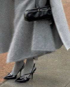 a woman in grey coat and high heels walking down the street with her handbag