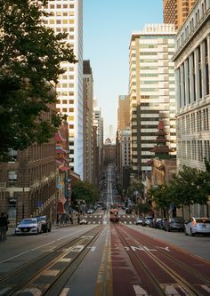 an empty city street with tall buildings on both sides and cars driving down the road