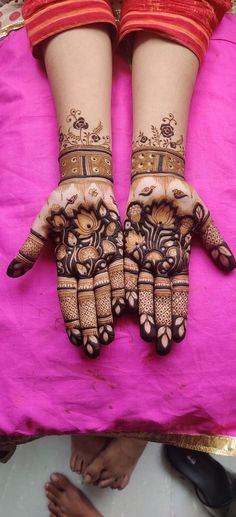 two hands with henna designs on them, sitting on a pink blanket in front of people