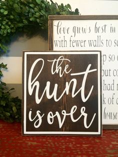 two wooden signs sitting next to each other on a red tablecloth covered shelf with greenery