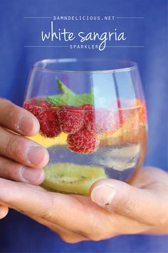 a person holding a wine glass filled with fruit and veggies, while the text reads white sangria sparkles