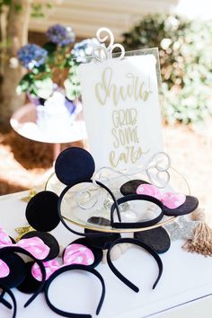 some minnie mouse ears are on top of a cake plate with a sign in the background