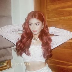 a woman with long red hair wearing a white crop top and silver sequin skirt