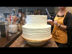 a woman in an apron is cutting a large white cake