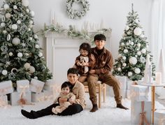 three children sitting on a chair in front of a christmas tree with presents around them