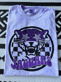 New product- Preppy Jaguars Mascot Shirt! Each shirt is meticulously printed by me using high-quality materials on a Comfort Colors shirt, known for its exceptional comfort and durability. Whether you're cheering on the Jaguars at the stadium or simply want to showcase your school spirit in your everyday attire, this shirt is the perfect choice. Available in Unisex sizes S to 3X, we've got you covered regardless of your preferred fit. The Preppy Jaguars Shirt features a classic crew neck and short sleeves with a fun splatter print! This preppy Jaguars shirt is a definite conversation starter and a unique fashion statement- wear it with jeans, shorts, or leggings for a casual and trendy look that showcases your Jags spirit! Note: As each shirt is individually printed, slight variations in c Cheap Shirt With Funny Print For School Spirit, Purple School Spirit T-shirt With Graphic Print, School Spirit Cotton Shirt With Graphic Print, Cotton School Spirit Shirt With Graphic Print, Purple Cotton T-shirt With Sublimation Print, Purple Graphic Tee With Screen Print, Trendy Purple Shirt With Graphic Print, Purple Cotton Shirt With Custom Print, Purple Cotton Top With Sublimation Print