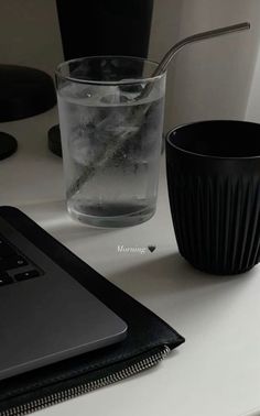 a laptop computer sitting on top of a desk next to a glass filled with water