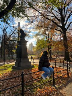 a woman sitting on top of a metal fence next to a park filled with trees