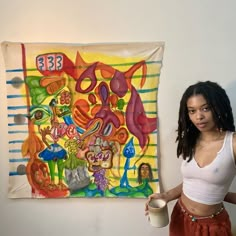 a woman standing in front of a painting holding a cup and looking at the camera