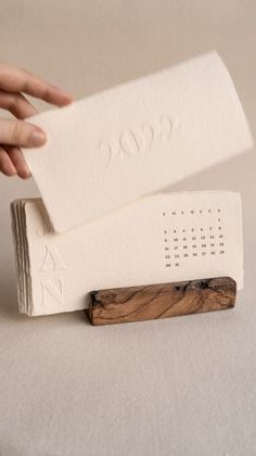 two white business cards sitting on top of each other next to a hand holding a piece of wood