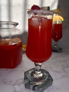 two glasses filled with red liquid and garnished with lemons on a marble table