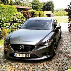 a car parked in front of a house on a cobblestone driveway with trees and bushes behind it