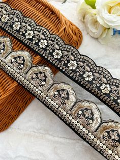 two black and gold beaded belts sitting on top of a wicker basket next to flowers