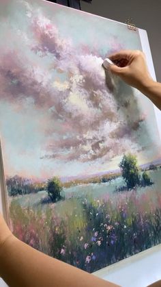 a woman is painting a landscape with pastel colors