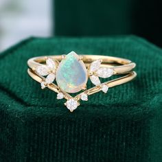 an opal and diamond ring sits on top of a green velvet cushioned box