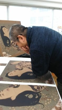 a man is looking at some paintings on the table with his head in his hands