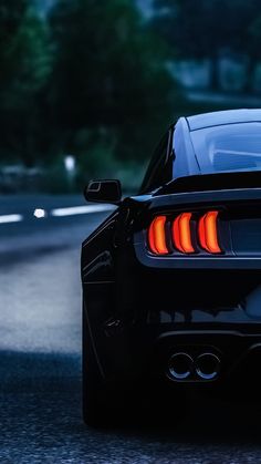 the rear end of a black sports car driving down a road at night with its lights on