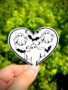 a hand holding up a heart shaped sticker with bats and ghostes on it